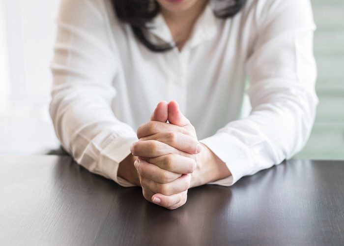 Closeup of a person's hands folded, resting on a table