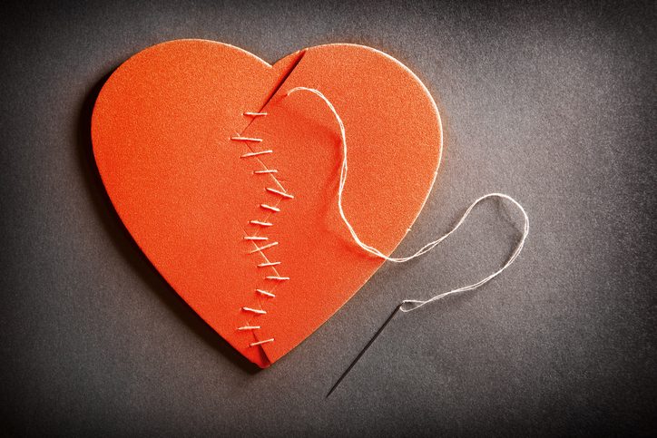 A broken heart with a needle and thread stitching it back together.