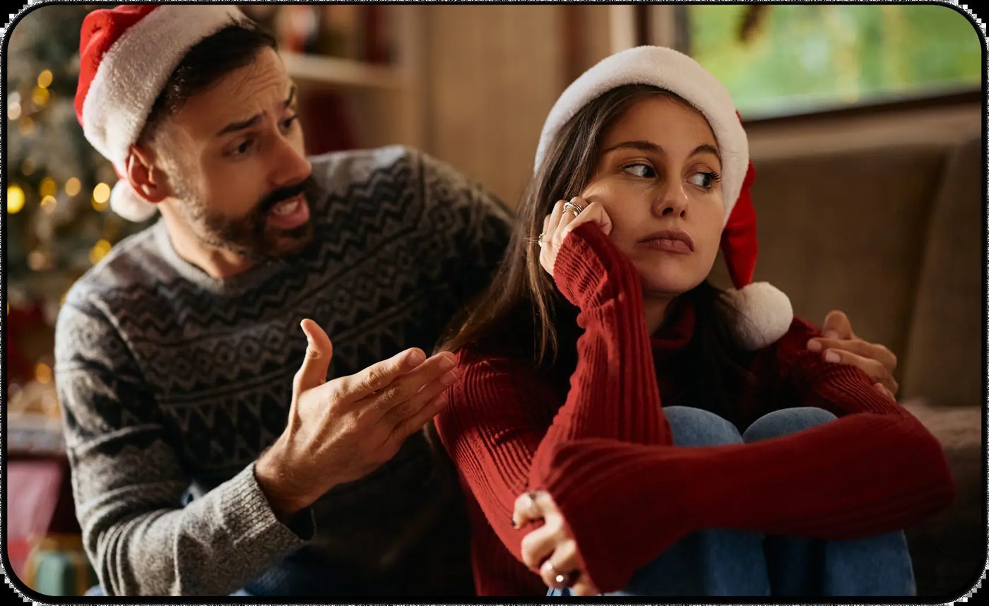 Couple in Santa hats arguing on the couch during holiday family conflict