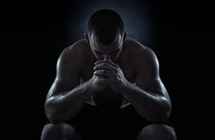 Young athlete on black background with face pressed to interlocked fingers