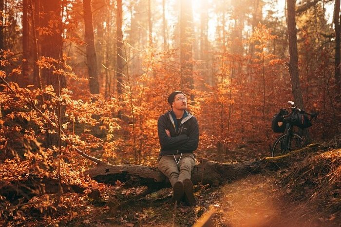 Man sitting on log in autumn forest with thoughtful expression