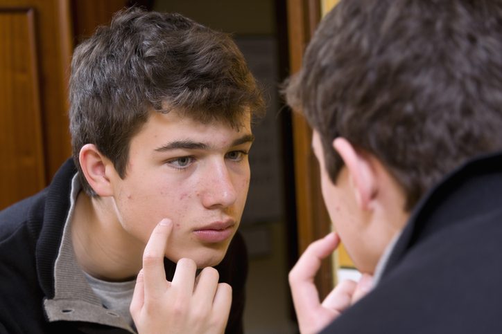 Teenager examining acne in the mirror