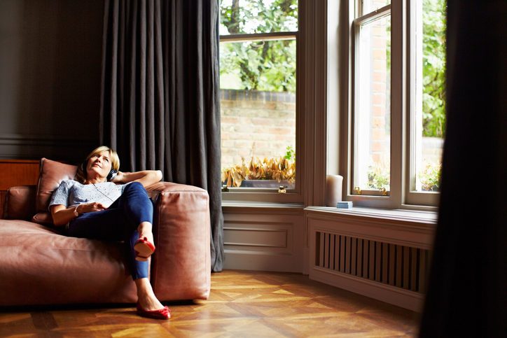 Shot of a mature woman lying back on her sofa listening to music on headphones