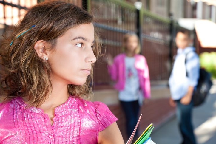 Teenager with short curly hair and pink shirt looks to side while walking away from two classmates standing together