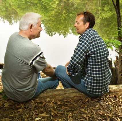 Father and adult son chat by a lake