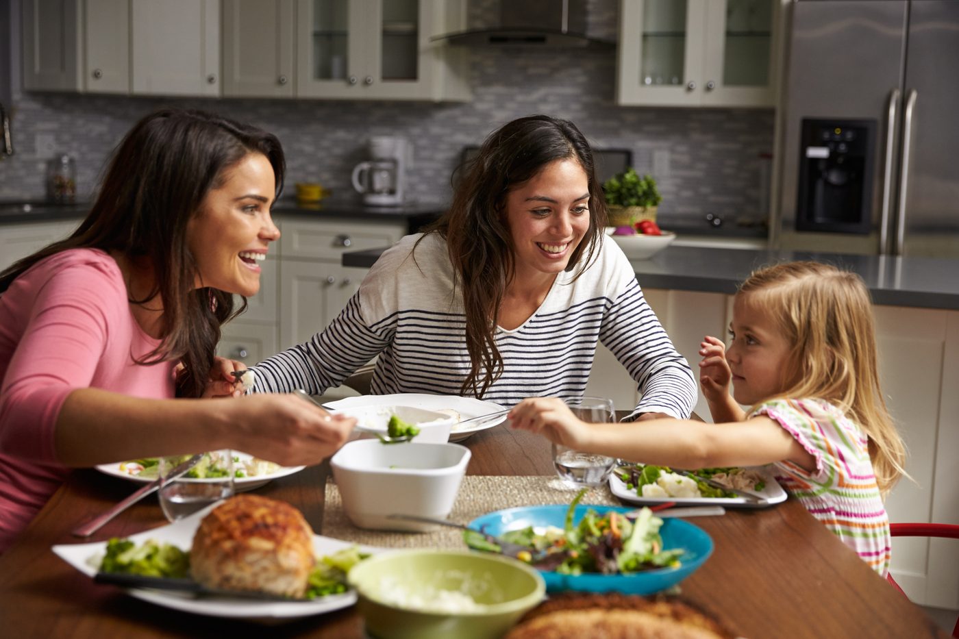 Two moms and daughter eating dinner