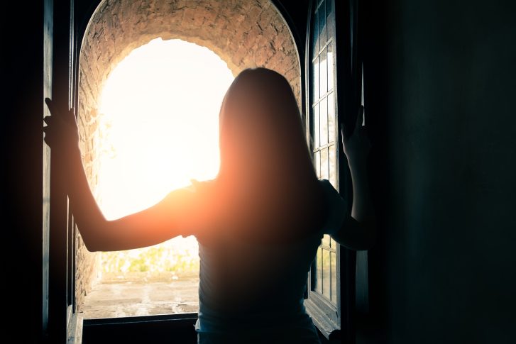 Woman opens window and looks out at sun