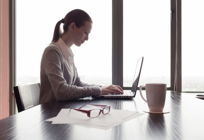 Side view of woman working at table with coffee and laptop